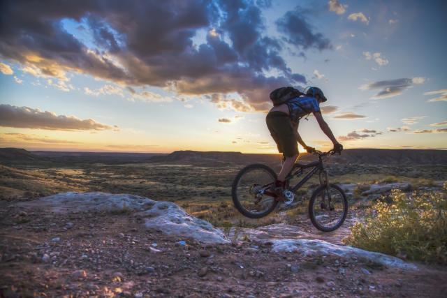 A person on a bike, rides along a trail at sunset.