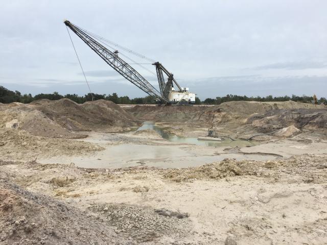 An image of a barren landscape with a construction crane in this middle of the phone and a puddle of muddy water in front of it