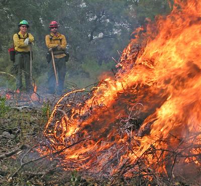two fire fighters observe a pile burn