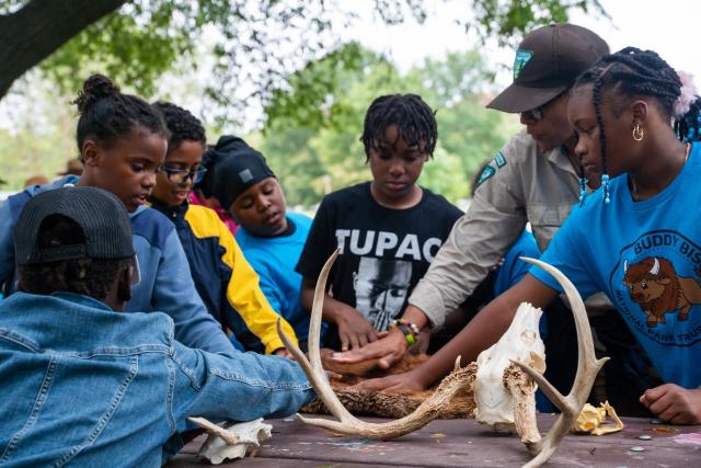 A woman and six children are touching animal fur that is on a table. 