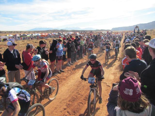 A crowd cheers on several bike racers on a dirt trail.
