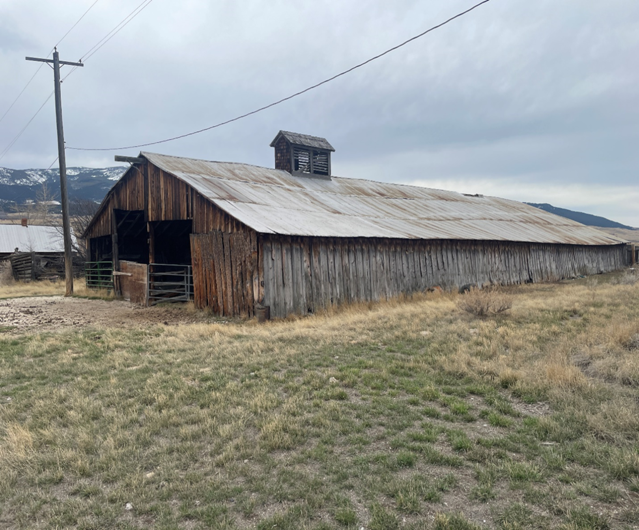 Rustic wooden barn with a weathered metal roof set in a grassy field under a cloudy sky.