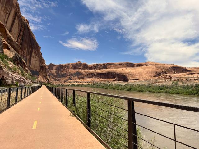 A paved bike path along a river and steep sandstone walls.