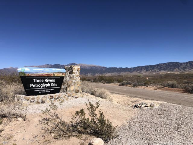 A Three Rivers Petroglyph sign with a mountain in the distance.