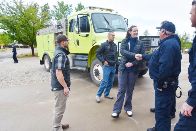 Smiling people shake hands in front of a very large, green fire truck