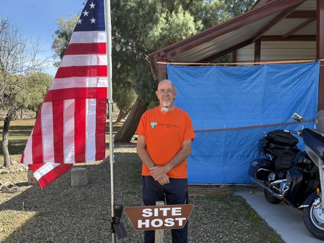 Volunteer stands next to a US Flag at the host site he serves from.