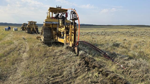 Three tractors using specialty plows bury power and fiber optic cable lines across a prairie landscape.