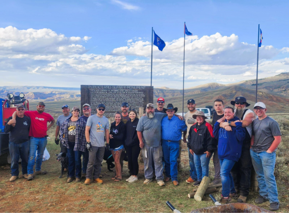 group of blm staff and volunteers stand for photo in front of marker with blue sky