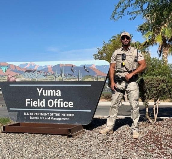 A uniformed law enforcement ranger stands to the right of the Yuma Field Office sign.
