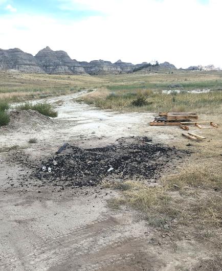 Pile of rubble and ash with pallets and buttes in background