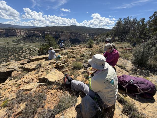 A small group of volunteers sit near an overlook of El Malpais National Conservation Area.