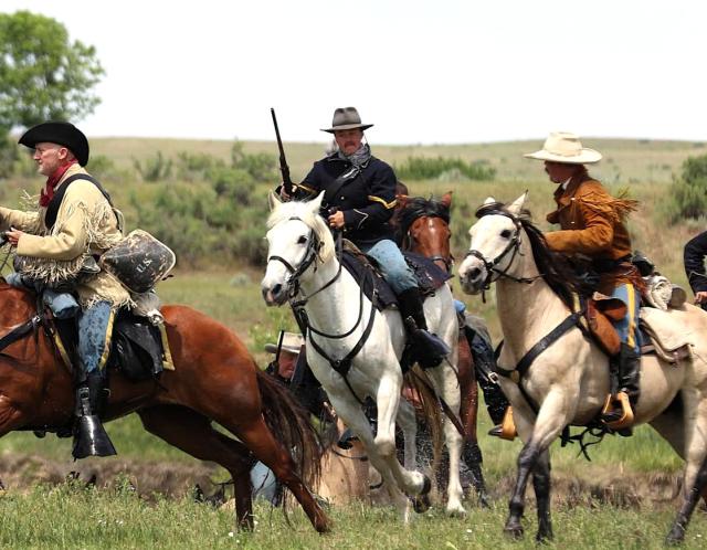 An individual on a white horse, surrounded by others on horses, all wearing historical period garb