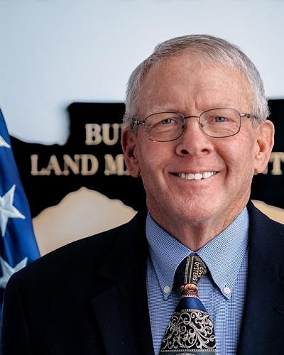 person with short hair wearing glasses and a tie posing in front of the American flag