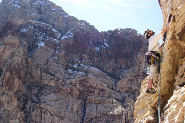 A rock climber in helmet and harness ascends a white cliff.