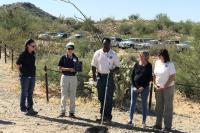 five people stand in a desert landscape. a woman holds a plaque