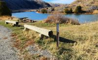 Log benches and a metal picnic table sit on the bank of a river.