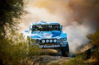 A blue truck drives through the dirt.