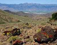 A large boulder in the foreground with a high desert valley and large blue mountains in the background .