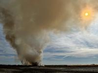 Plume of smoke rising over the sun in the desert.