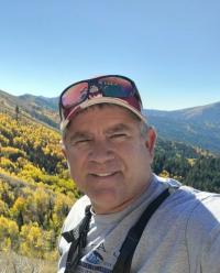 Photo of Blaine Newman hiking, with mountains and blue sky in the background.