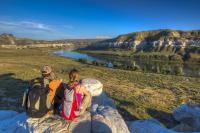 Two people in hiking gear sit on a rock ledge overlooking a river