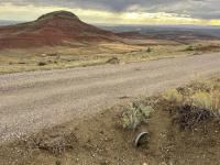 A gravel road with a culvert at its base runs past a scenic red mesa.