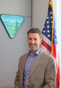 Man stands in front of US Flag and BLM Logo wearing suit jacket