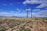 Powerline spanning across a brushy flat area with blue skies and a few white clouds in the distance.