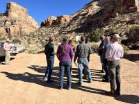 A group of people stand around a map in front of a desert canyon.