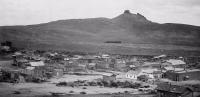 An Old West mining town with wooden building in the foreground and a hill in the distance.