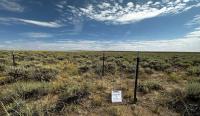 a fenced area is shown on a sagebrush and grass landscape with blue skies