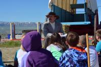 A man in 19th century clothing presents to a group of children. 