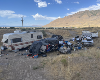 A camper and a vehicle are pictured among piles of debris and trash 