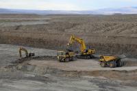 An excavator loads material into a large dump truck as another dump truck waits to be loaded.