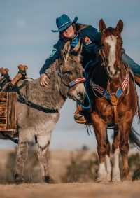 A woman poses for a photo with a horse and burro wearing a cowboy hat.