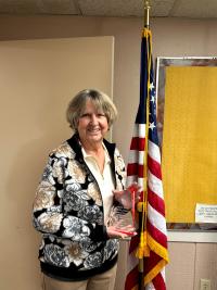 Mona Daniels stands with an award near an american flag indoors.