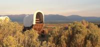 A covered wagon surrounded by sage brush with distant mountains at sunset