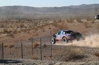 A blue and orange trophy truck speeds through the desert.