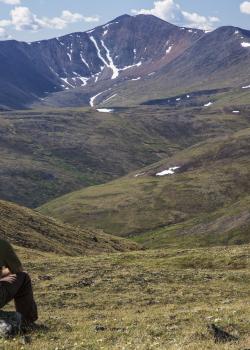 Hiker sitting on rock overlooking the mountains of the Steese National Conservation area in Alaska