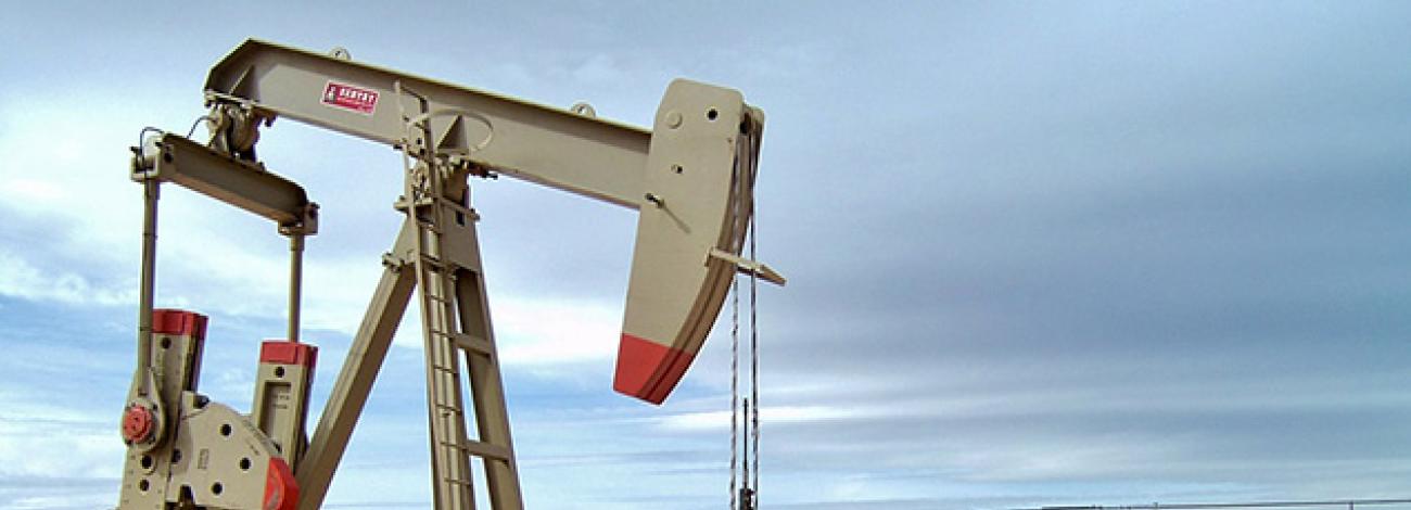 An oil pump jack in the foreground with three large storage tanks in the background