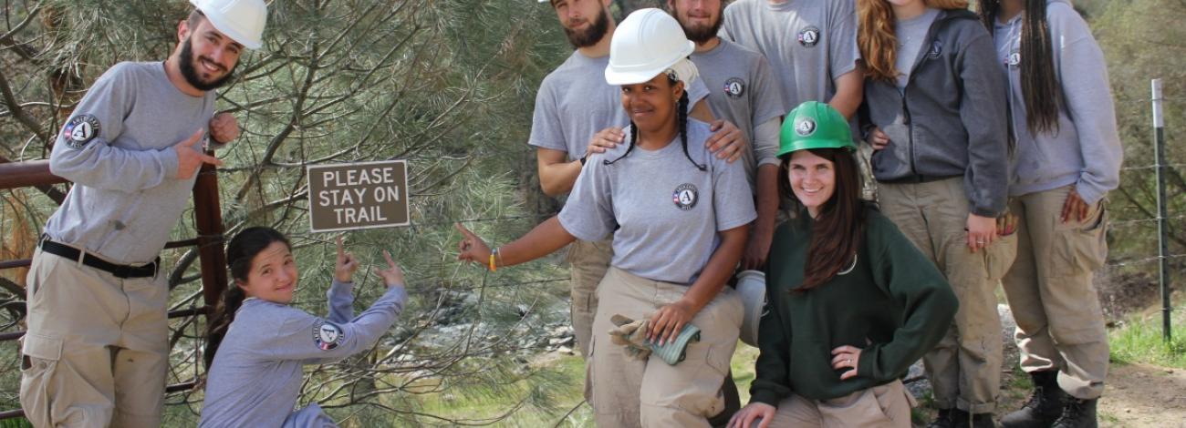 Group of AmeriCorps wearing hard hats and posing for group photo during trail work.