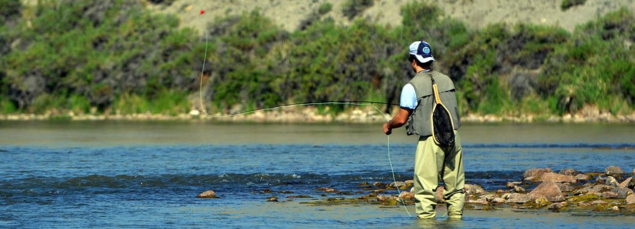 a person wearing a fishing vest and waders casting with a fly fishing rod.