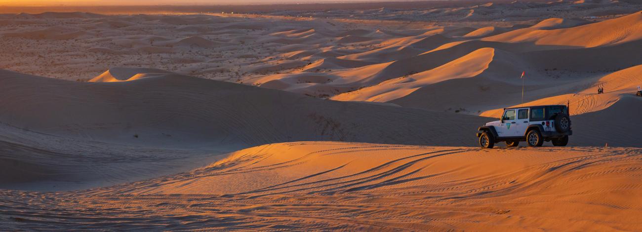 A jeep overlooks a sea of dunes at sunset