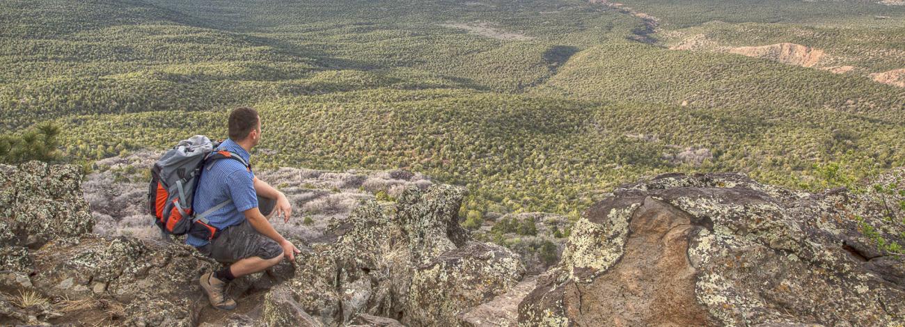 A hiker kneels on a cliff edge overlooking the Grand Canyon-Parashant National Monument.