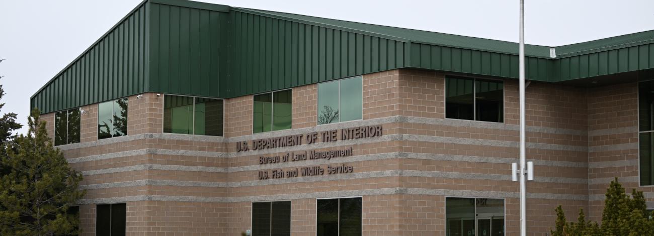 A brick building that is home to the Nevada State Office for the Bureau of Land Management located in Reno, Nevada sits behind the U.S. flag as the sun rises.