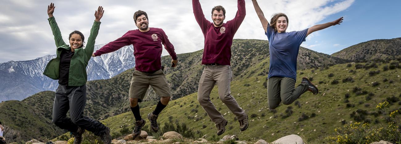 Four people jump in the air in celebration with a mountainous landscape in the background.