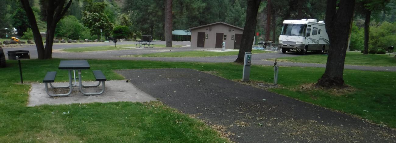 Recreational vehicle site at Mckay's Bend Campground. Grass, picnic bench in foreground.  RV and bathrooms in background.