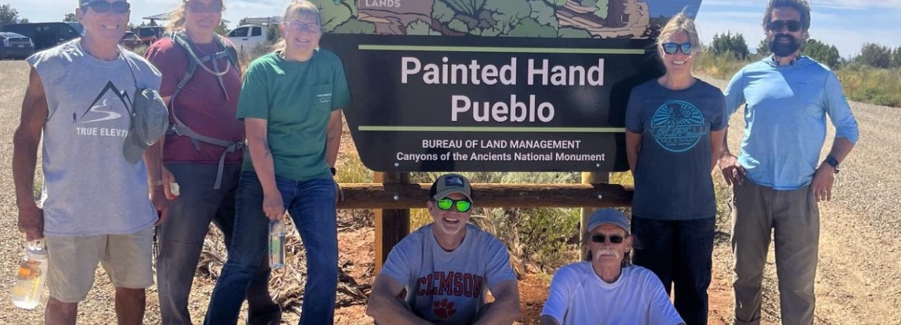 Volunteers pose in front of a sign after completing work at Painted Hand Trailhead in Canyons of the Ancients NM on National Public Lands Day 2023.