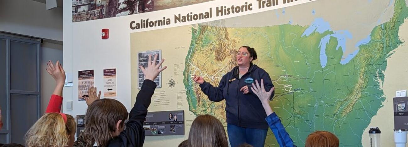 Students raise their hands to be called on by an educator in front of a map of the Oregon Trail
