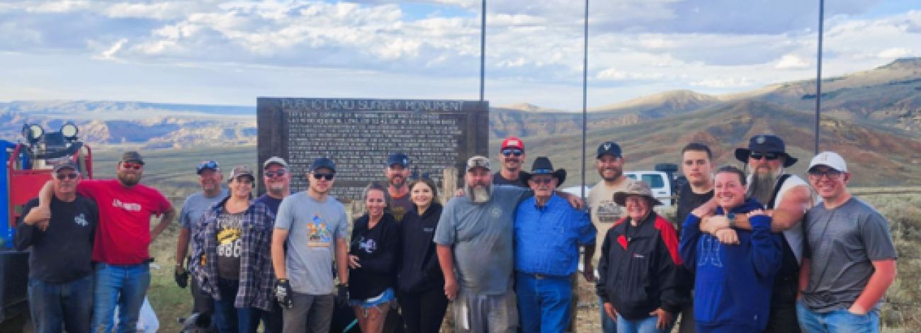 group of blm staff and volunteers stand for photo in front of marker with blue sky